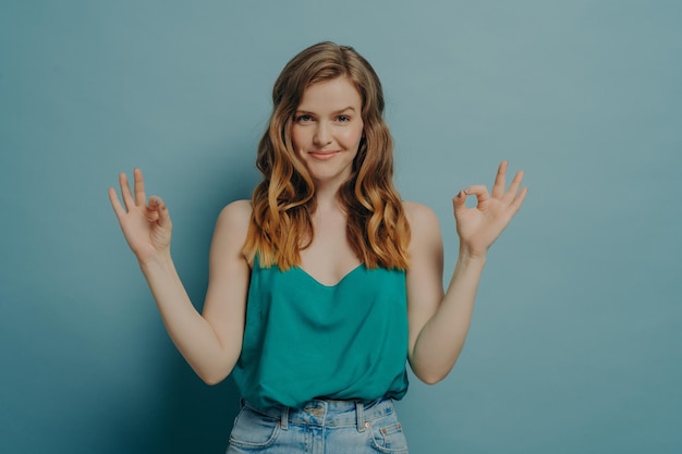 Zelfverzekerde vrolijke jonge vrouw in casual kleding gebaren ok teken met beide handen in studio