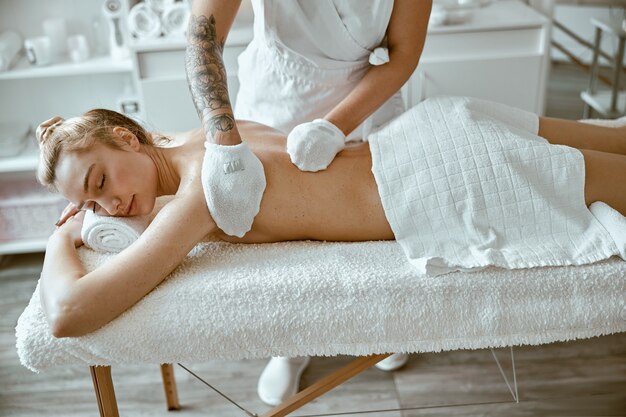 Zelfverzekerde vrouwelijke specialist doet ontspannende lichaamsmassage voor mooie slanke blanke dame in minimalistische spa-salon