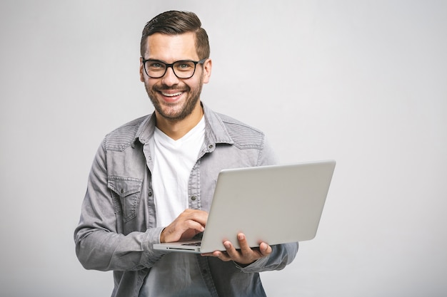 Zelfverzekerde zakelijke expert. Zekere jonge knappe mens in laptop van de overhemdsholding, camera bekijkt en glimlachend terwijl status tegen witte achtergrond