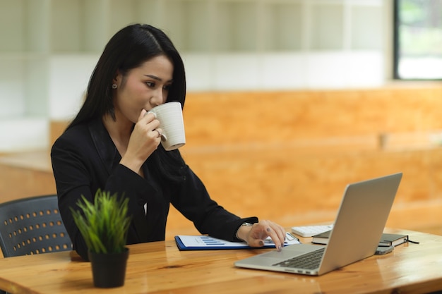 zelfverzekerde zakenvrouw die koffie drinkt tijdens het werken op een laptop slimme zakenvrouw