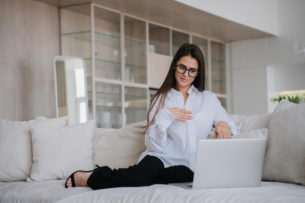 Foto zelfverzekerde zakenvrouw in bril, wit overhemd en zwarte broek maakt videogesprek met laptop