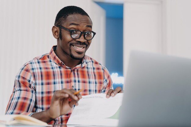 Foto zelfverzekerde zwarte man met een bril die een videogesprek maakt op zijn laptop