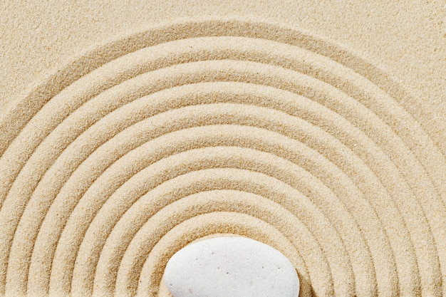 Zen garden meditation sandy background with stone cairn and round lines on sand