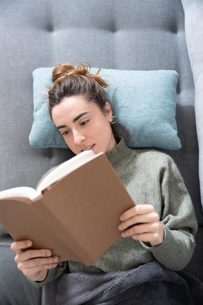 Zenitale weergave van jonge student die een boek leest terwijl hij op de bank ligt