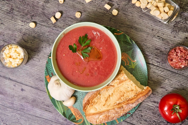 Zenithmening van een gazpachokom met peterselie en extra vergine olijfolie vergezeld van brood en knoflook rond zijn er croutons serranoham-ei en een tomaat concept van mediterraan voedsel