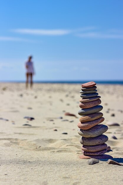 Zenpiramide van balancerende stenen op een zandstrand met een vrouw die op de achtergrond loopt Selectieve focus