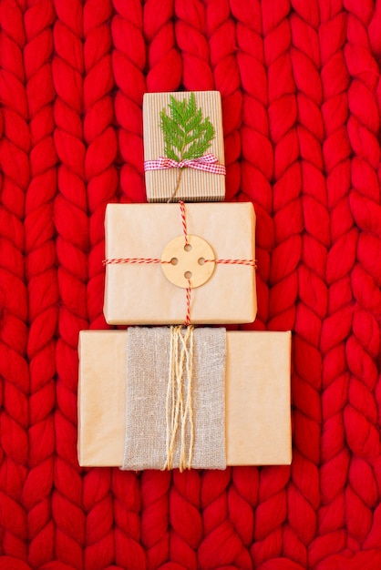 Безотходные рождественские подарочные коробки с натуральными рождественскими украшениями, завернутые в безпластиковую крафт-бумагу в форме рождественской елки на мягком вязаном одеяле из шерсти мериноса ручной вязки. Концепция эко-декора.