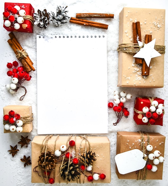 白い雪の背景に装飾が施されたプレゼントとゼロウェイストクリスマステキスト。ノートブックの空のコピースペース。クラフトダンボールのタグが付いた環境にやさしいパックギフト。新年