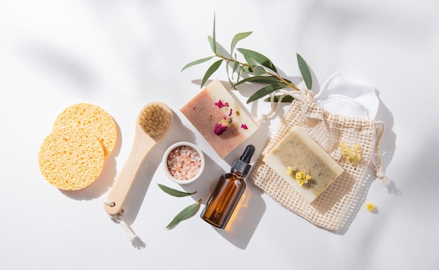Zero waste concept beauty spa  with natural cosmetic products: soap, sponges, oil  and massage brushes, mineral salt on white  background with hard shadows and flowers.  Top view and copy space image