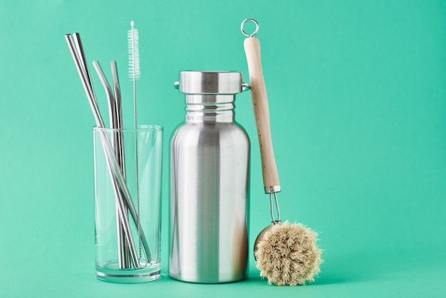 Zero waste concept. Eco friendly reusable items aluminun bottle and metal tubes in glass on green