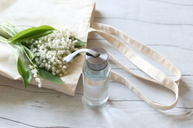 Zero waste concept. Glass water bottles and eco bag on a white wooden table.