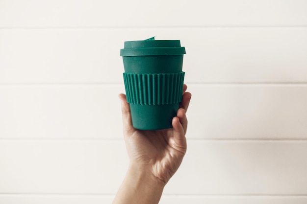 Zero waste concept Hand holding stylish reusable eco coffee cup on white wooden background Green Cup from natural bamboo fiber Ban single use plastic Make a choice