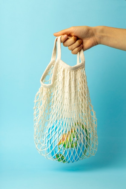 廃棄物ゼロのコンセプト。地球と女性の手で文字列のバッグ。ビニール袋無料