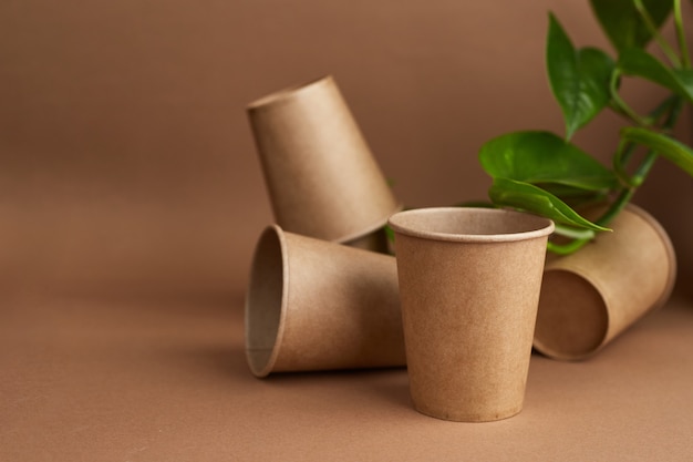 Zero sprechi. bicchieri di carta usa e getta con foglie verdi. caffè ed ecologia. sfondo beige