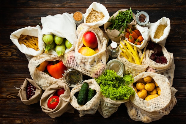 Zero waste shopping en bewust consumptieconcept. Verschillende soorten voedsel in herbruikbare verpakkingszakken en glazen potten op de houten tafel, bovenaanzicht