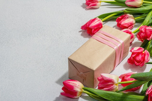 Zero waste spring gift concept Pink tulips surprise paper box for Anniversary Mothers or Valentines Day Happy birthday greeting card light stone concrete background copy space