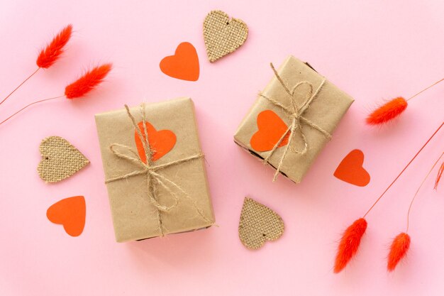 Zero waste valentine's day flat lay. Gift boxes wrapped in craft paper with hearts and spikelets on pink wall.