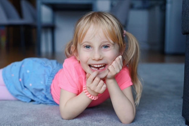 Zes jaar lachend gelukkig meisje dat een eerste gevallen tand vasthoudt en naar hem kijkt