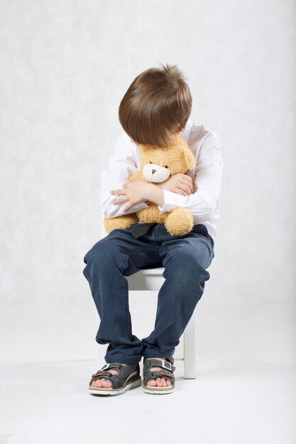 Zes jaar oude jongen zittend op de stoel met pluche teddybeer. Detailopname