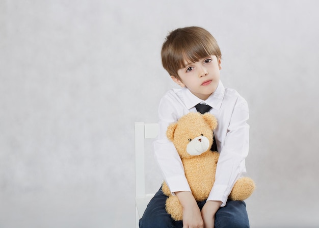 Zes jaar oude jongen zittend op de stoel met pluche teddybeer. Detailopname