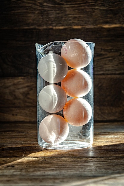 Zes witte kippeneieren in een glazen kolf op een houten keukentafel.