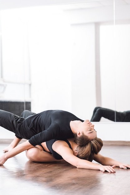 Zich baserend op de partner. Leuke goed uitziende hardwerkende vrouw zittend in kleermakerszit op de grond en voorover buigend terwijl ze haar partner op haar rug houdt