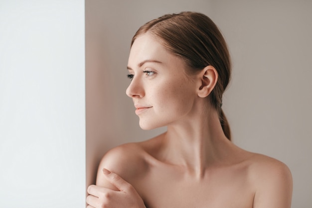 Zich mooi voelen. Aantrekkelijke jonge vrouw met sproeten op het gezicht die wegkijkt en de hand op de schouder houdt