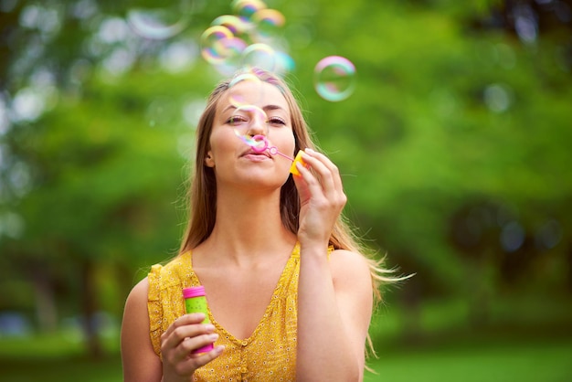 Zich overgeven aan haar innerlijke kind Shot van een zorgeloze jonge vrouw die bellen blaast in het park