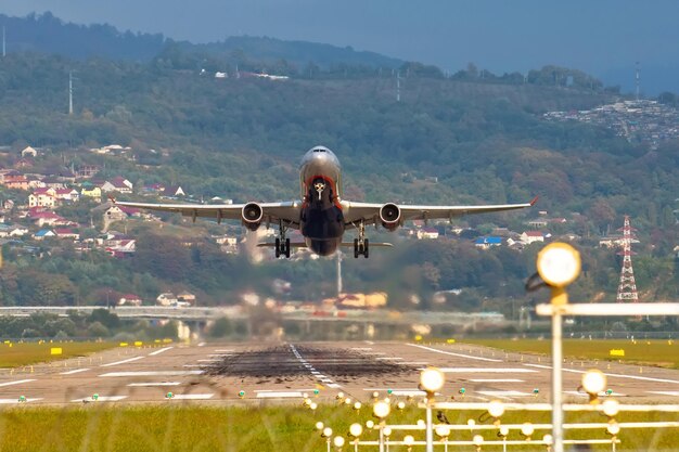 Zicht op de landingsbaan van de luchthaven en een opstijgend vliegtuig tegen de achtergrond van bergen en huizen