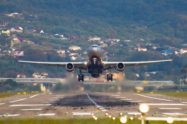 Zicht op het einde van de landingsbaan van de luchthaven en een opstijgend vliegtuig tegen de achtergrond van bergen en huizen