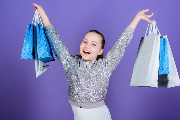 Zie er beter uit Zwarte vrijdag Verkoopkorting Winkeldag Kind houdt bospakketten Kindermode Verjaardag meisje Verrassingscadeau Meisje met boodschappentassen violette achtergrond Winkelen en kopen