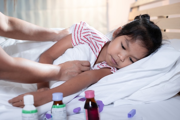 Ziek Aziatisch kindmeisje ligt op bed en haar moeder zorgt voor en bedekt de deken op haar dochter