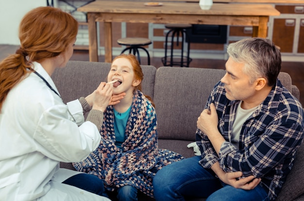 Ziek kind. Schattig roodharig meisje zit voor de dokter terwijl haar keel wordt gecontroleerd