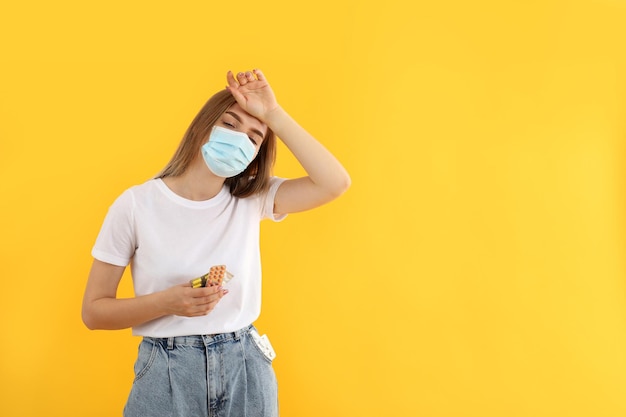 Ziek meisje in masker met pillen op gele achtergrond