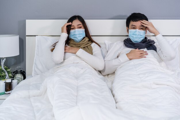 Ziek paar in medische masker hoofdpijn en lijden aan virusziekte en koorts in bed, coronavirus pandemisch concept.