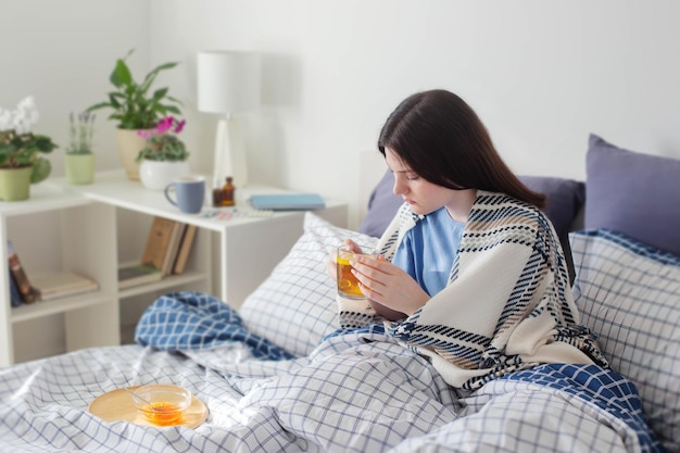 Ziek tienermeisje met thee op bed in witte kamer