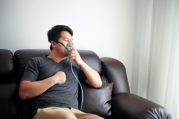 Zieke Aziatische jongeman die thuis een vernevelaar gebruikt voor astma en luchtwegaandoeningen