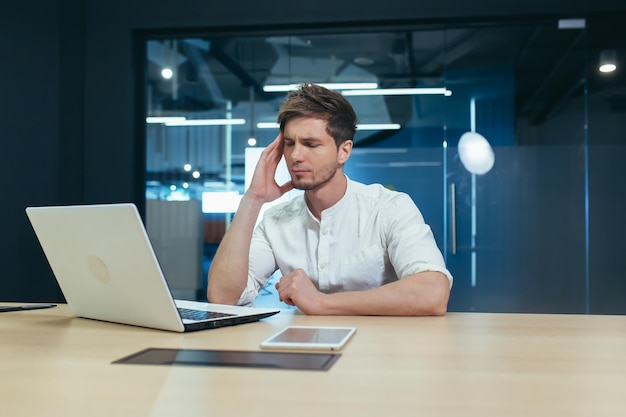 Zieke en vermoeide man die op kantoor werkt met een laptop heeft een ernstige hoofdpijn overwerkte zakenman werknemer