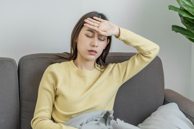 Zieke griep aziatische jonge vrouw meisje hoofdpijn heb koorts griep en controleer thermometer meet lichaamstemperatuur voel ziekte thuis zittend op de slaapbank Gezondheidszorg persoon op virus covid19