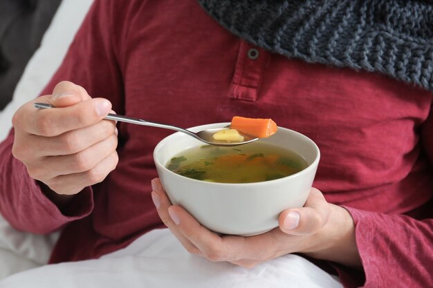 Foto zieke jonge man die bouillon eet om verkoudheid thuis in bed te genezen