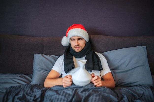 Zieke jonge man in rode kerstmuts zit op het bed