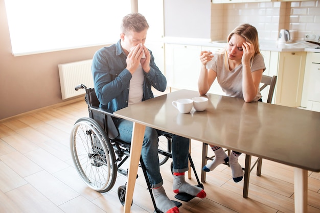 Zieke jonge man met inclusiviteit niezen met gezonde vrouw aan tafel