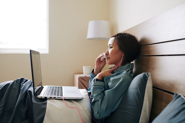 Zieke jonge Vietnamese vrouw die in bed ligt en haar arts belt