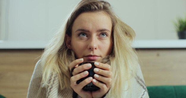 Zieke jonge vrouw drinkbeker met hete thee terwijl ze thuis op de bank zit. Concept van gezondheidszorg en ziekte.