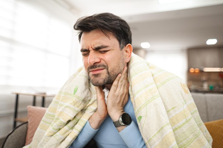 Foto zieke man bedekt met een deken zit en houdt zijn zieke keel vast