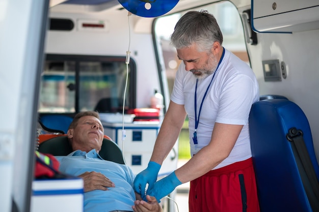 Foto zieke man liggend op de brancard terwijl een ervaren arts de katheter in zijn ader inbrengt