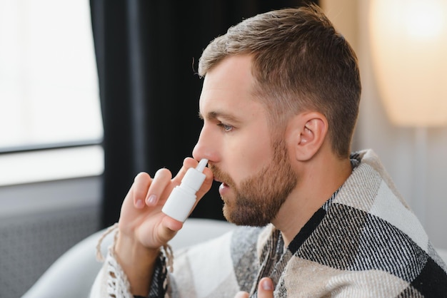 Foto zieke man met neusspray en papieren zakdoekje thuis