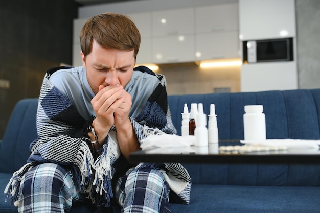 Foto zieke man op de bank thuis in de woonkamer man ziek van kou en koorts thuis ziek van griep zittend op de bank het is het seizoen van niezen