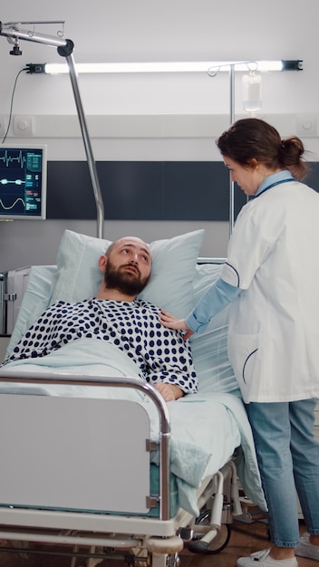 Zieke man rust in bed terwijl de therapeut arts het ademhalingsherstel bewaakt terwijl hij op de ziekenhuisafdeling werkt