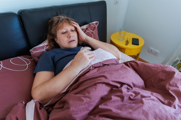 Foto zieke oude vrouw die thuis in bed ligt, voelt zich ziek, lijdt aan griep of verkoudheid, geneest met medicijnen